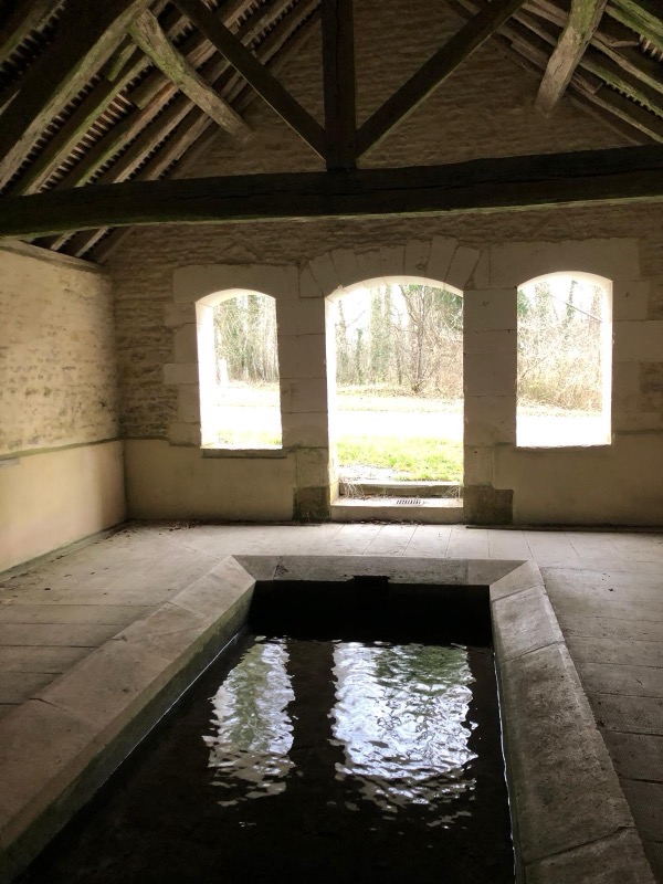 Intérieur du lavoir de Baon, bassin en pierre calcaire et charpente en bois