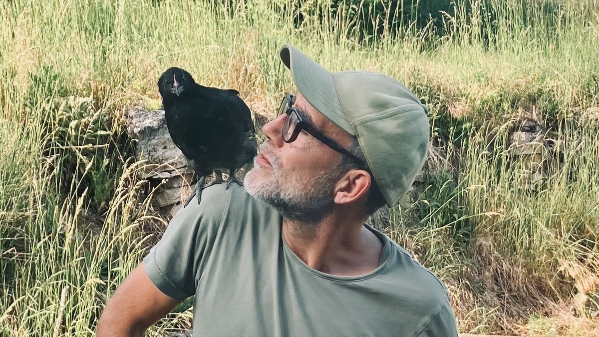 Une jeune Noire de Janzé perchée sur l'épaule de son propriétaire dans le jardin de Baon, feuillage vert en arrière-plan