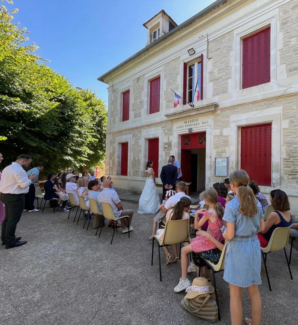 Cérémonie de renouvellement des vœux devant la mairie de Baon, invités assis et mariés au centre.